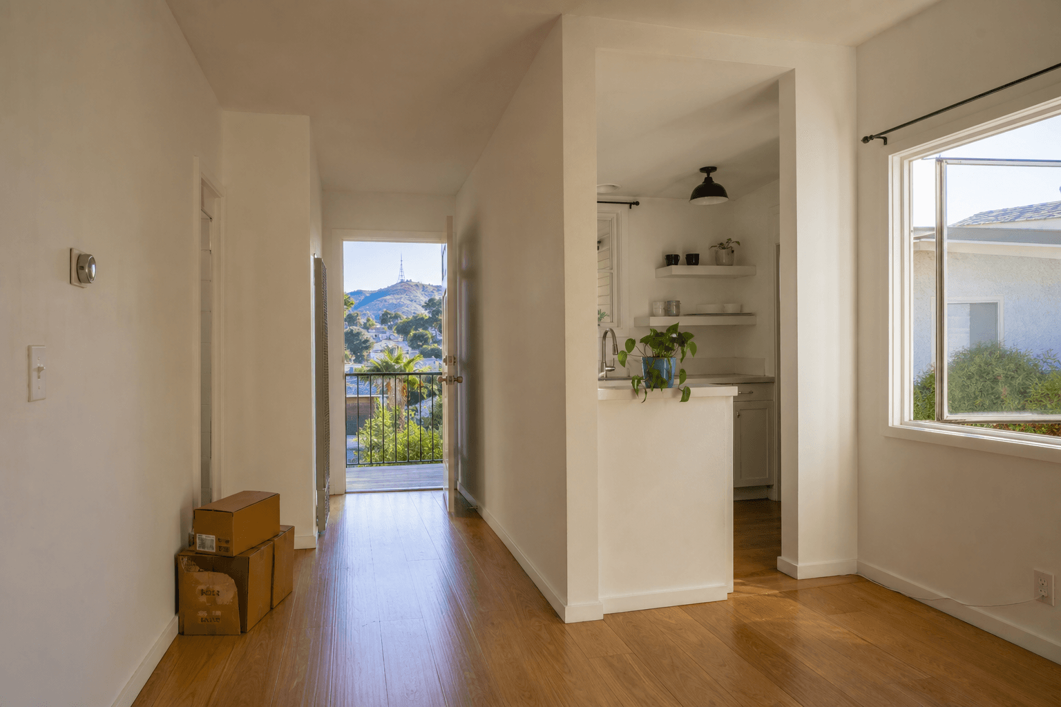 Freshly turned mid-century LA apartment with clean white walls, hardwood floors, and open windows showing hills
