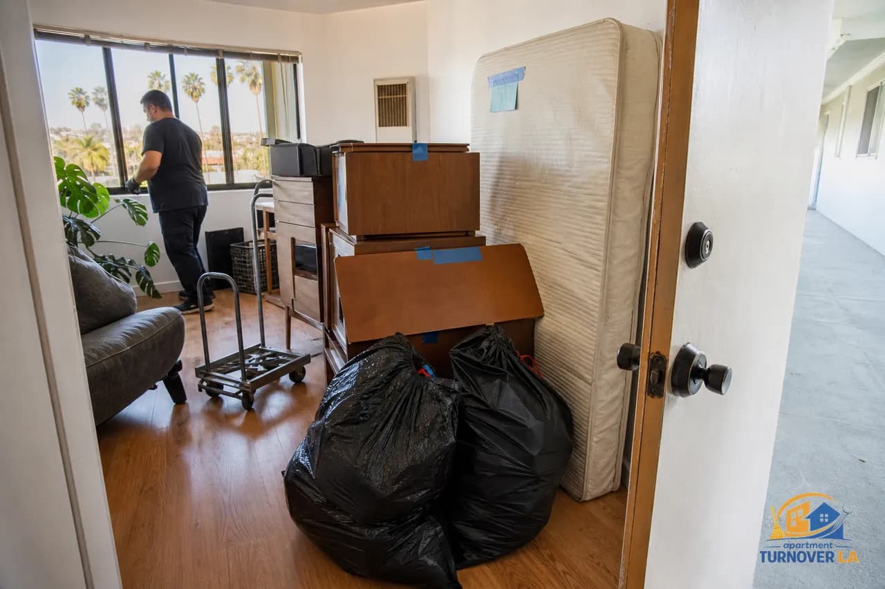 LA apartment junk cleanout with bagged trash, tagged mattress, and dolly staged by the door in soft morning light